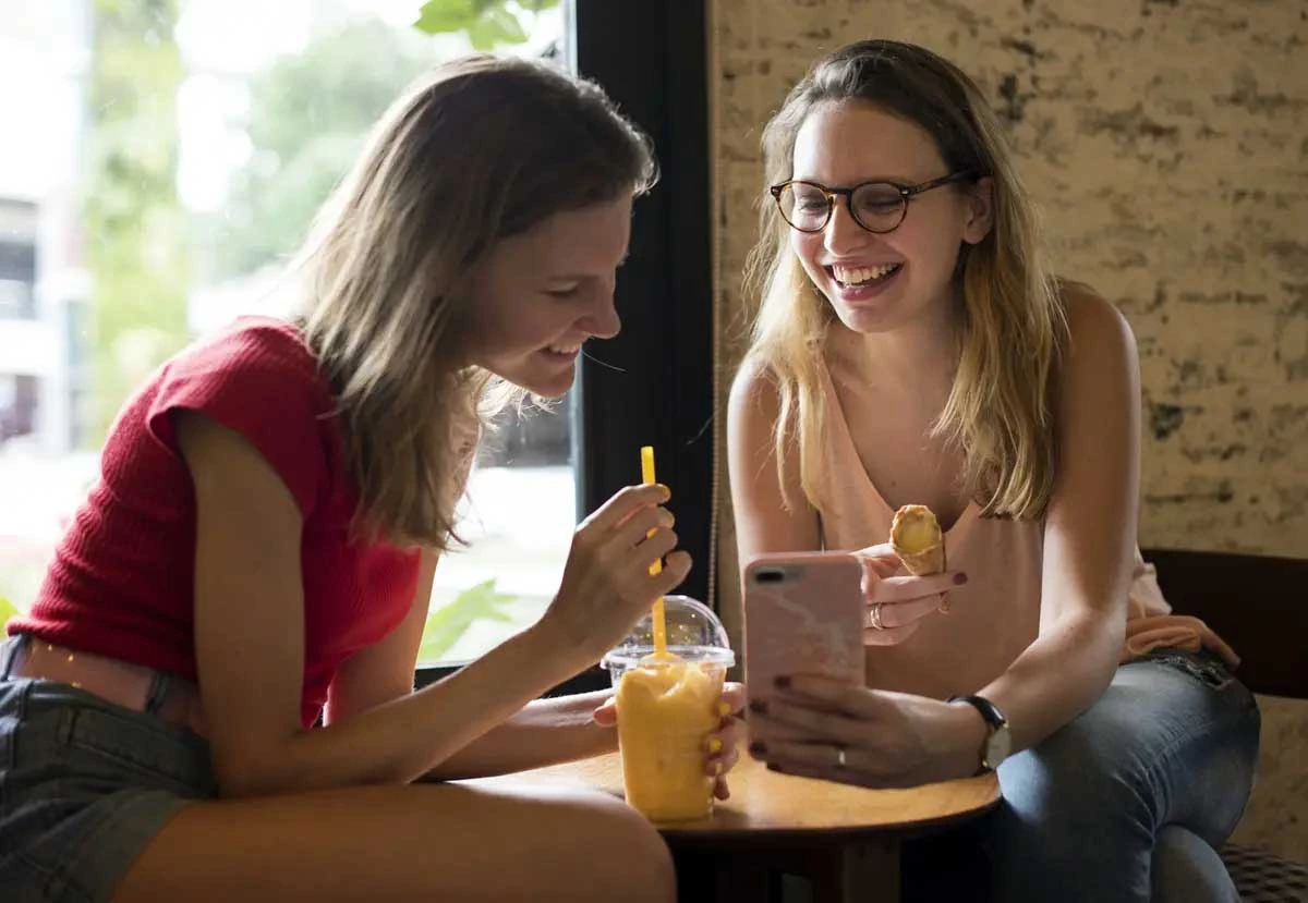 Two students having a snack while looking at a cell phone